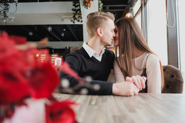 Young couple in love, man and woman on a romantic date in a cafe. Sit at a table by the window. On the table a bouquet of red flowers.
