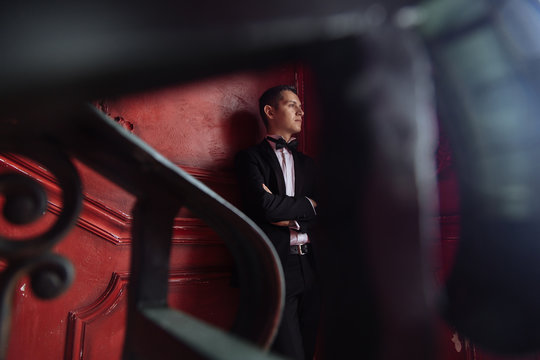 Photo Of Elegant Thoughtful Young Man In A Suit, On A Dark Red Background, Looking Away From The Camera