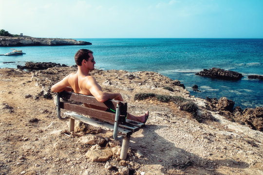 Rear view portrait of white man sitting relaxed on a bench and looking at the sea, man on a holiday. Cyprus