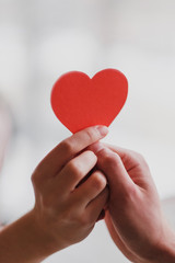 Obraz premium Male and female hands hold a valentine in the form of a paper heart.