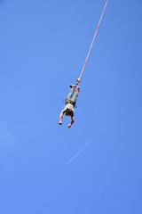 Bungee jumping from crane during Sofia Extreme Sports Festival. Man hanging on a cord high in the blue sky. White airplane trail seen at distance 