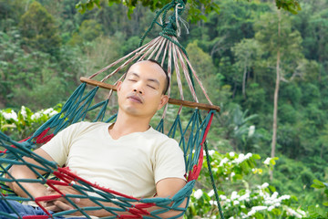 Asian man is sleeping on a hammock among nature