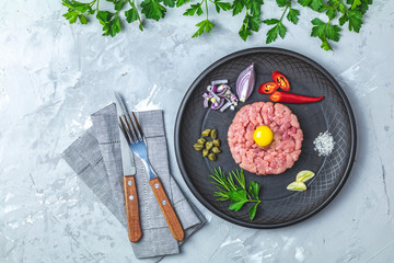 Steak tartare with yolk and ingredients on black ceramic plate