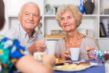 Smiling elderly spouses enjoying tea with girl