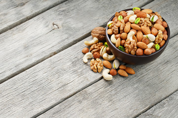Wooden bowl with mixed nuts on a wooden gray background. Walnut, pistachios, almonds, hazelnuts and cashews, walnut.