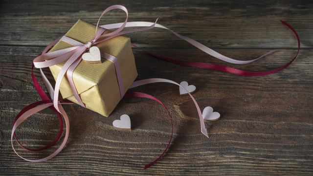 Valentinsgeschenk, Verlobungsgeschenk mit rosa Schleife und Herzchen auf rustikalem Holzuntergrund