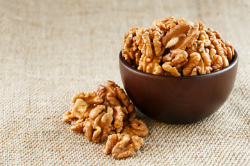 Peeled walnuts in a wooden, dark brown cup on a burlap cloth.