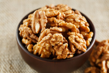 Peeled walnuts in a wooden, dark brown cup on a burlap cloth.