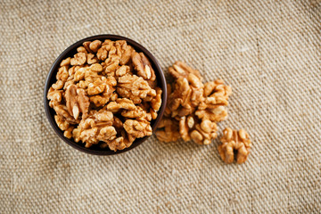 Peeled walnuts in a wooden, dark brown cup on a burlap cloth.