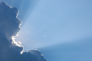 light rays of sun shine through big cloud above clear blue sky