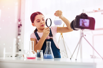 Dark-haired schoolgirl holding magnifying glass looking at blue substance