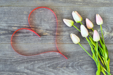 Tulips with pink tint with ribbon in the form of a heart of the color of living coral on a wooden vintage background.