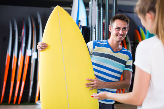 man is showing  to woman colorful boards in store on the beach.