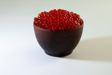 red caviar in a ceramic dish on a wooden platform on a white background