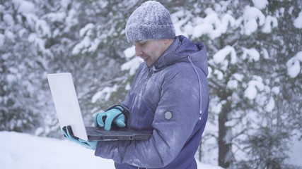 Portrait frozen man in winter forest uses laptop