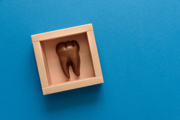 Tooth from chocolate in box on blue paper background. Top view. Copy space. Healthy teeth or  dental care concept