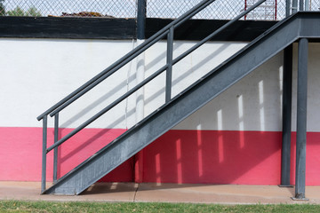 Metal staircase against a white and pink wall with a wire fence on top