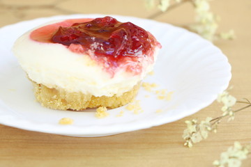close up one piece of strawberry cheesecake with red strawberry sauce , side view on wooden table background with little white flower