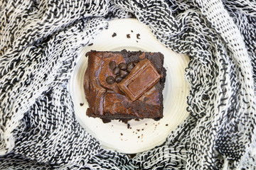 close up one piece of chocolate brownie with chocolate chip on white plate on fabric background, top view, vintage style