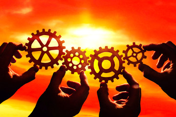 gears in the hands of people on the background of the evening sky. the concept of teamwork. the...