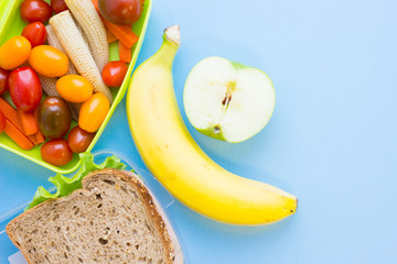 School lunch box. Bread, apple, candies, baby corns, carrot and tomatoes in green plastic container