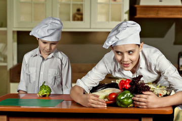 Boys in the cooks costumes cut the salad in the kitchen. Boy took all the food from another guy....