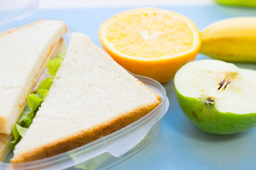 School lunch box. Bread, apple, candies, baby corns, carrot and tomatoes in green plastic container