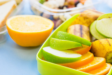 School lunch box. Bread, orange, candies, baby corns, carrot and tomatoes in green plastic container