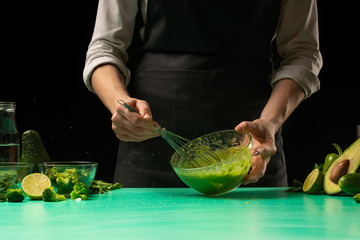 Chef on a black background makes cooking a green detox smoothie. Healthy, clean food, weight loss food concept