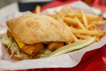 Deep fried fish sandwich on sour dough bun with cheese and lettuce.  Sandwich and fries in red basket with white paper liner.  Pickle included.