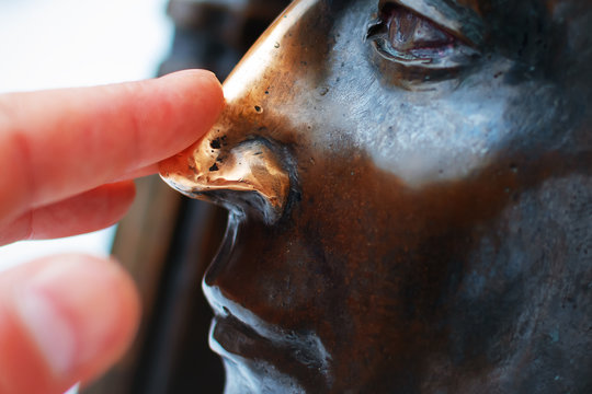 tourist rubs nose copper statue for good luck