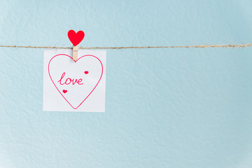 Red Valentine's love heart pin hanging on natural cord against blue background. drawn heart on...