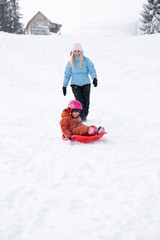 Fototapeta na wymiar Mom and daughter ride on a sled from a snow slide. Ride from a snow hill on a sled. Sleigh rides, winter fun, snow, family sleigh rides.
