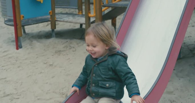 Little toddler coming down a slide at the playground