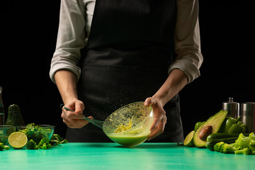 Chef on black background whips juice from vegetables for cooking green detoxification smoothies. Healthy, clean food, weight loss food concept, sport