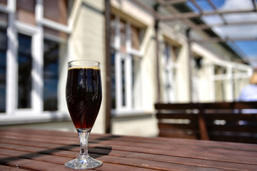 On a sunny day in an outdoor cafe, there is a glass of beer on the table. Selective focus.