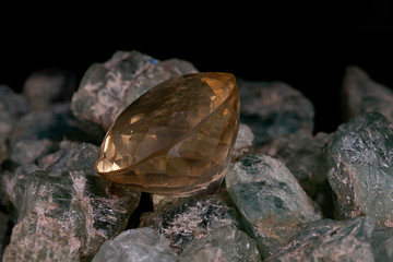 Close up of a variety of uncut green tinted gem stones with rough surfaces and on top of it a crafted yellow diamond shaped stone against a black background