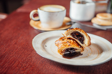 Puff pastry bun with liquid chocolate inside, lies in a plate on a dark wooden table in a cafe