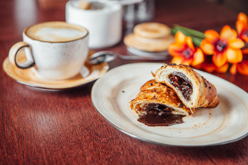 Puff pastry bun with liquid chocolate inside, lies in a plate on a dark wooden table in a cafe