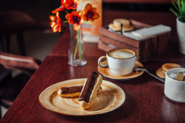 Chocolate eclairs lie in a plate on a dark wooden table in a cafe