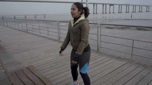 Smiling hindu woman with ponytail training outdoor. Attractive young lady wearing sport clothing during morning workout on wooden jetty. Concept of sport