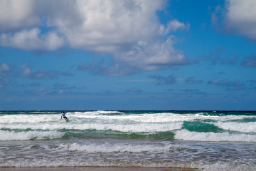 Surfer riding in low white waves in a blue background and clouds Fistral Beach Newquay England UK