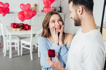 selective focus of surprised girl touching face while man doing proposal at valentines day