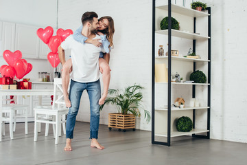 young man giving piggyback ride to smiling girlfriend in furnished room with st valentine day...