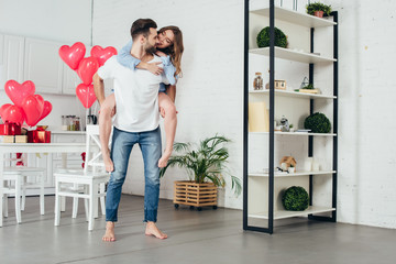 young man giving piggyback ride to smiling girlfriend in furnished room with st valentine day decoration