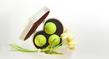 tennis love layout tennis balls in box in shape of heart with bouquet white tulips on white background. Women's Day March 8. Copy space. Valentine's day concept with tennis play. Flat lay, horizontal.