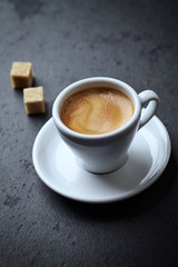 Cup of coffee and two brown sugar cubes on black stone background. Copy space.