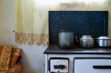 Old stove cooking pot and kettle black with curtain and patchy white wall