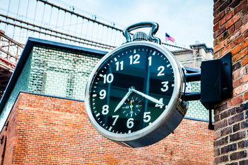 Stylish public analog clock hanging on brick wall showing time in Brooklyn, New York, USA during daytime