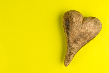 Wooden heart isolated on yellow background with clipping path and copy space on the left, view from the top.